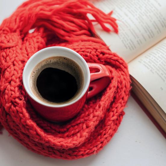 en kop kaffe med et halstørklæde omkring ved siden af en åben bog